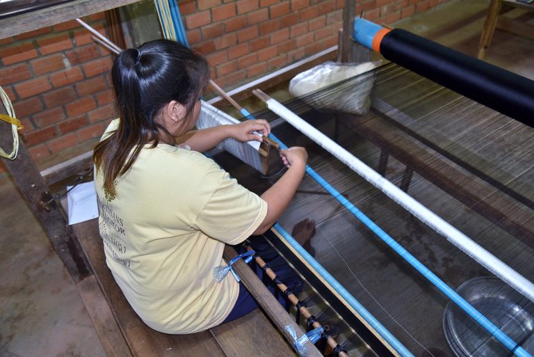 A weaver at a wooden loom threading silk at Artisans Angkor, Siem Reap.