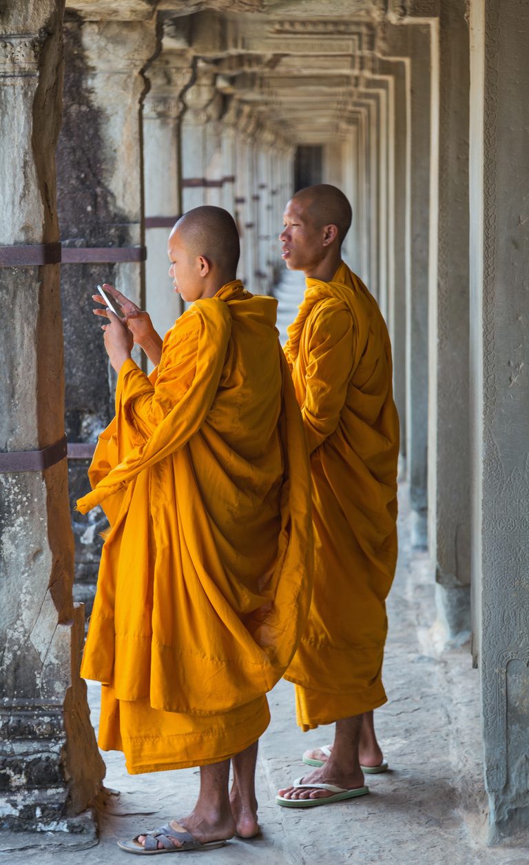 Two adult monks in saffron robes in a stone gallery at Angkor Wat.
