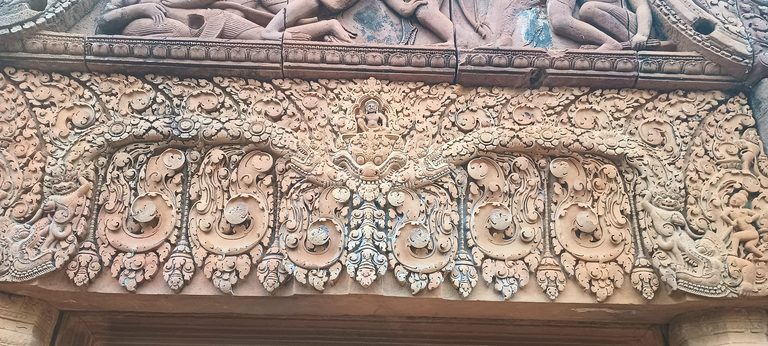 Intricate pink-sandstone lintel carved with foliage and figures at Banteay Srei.
